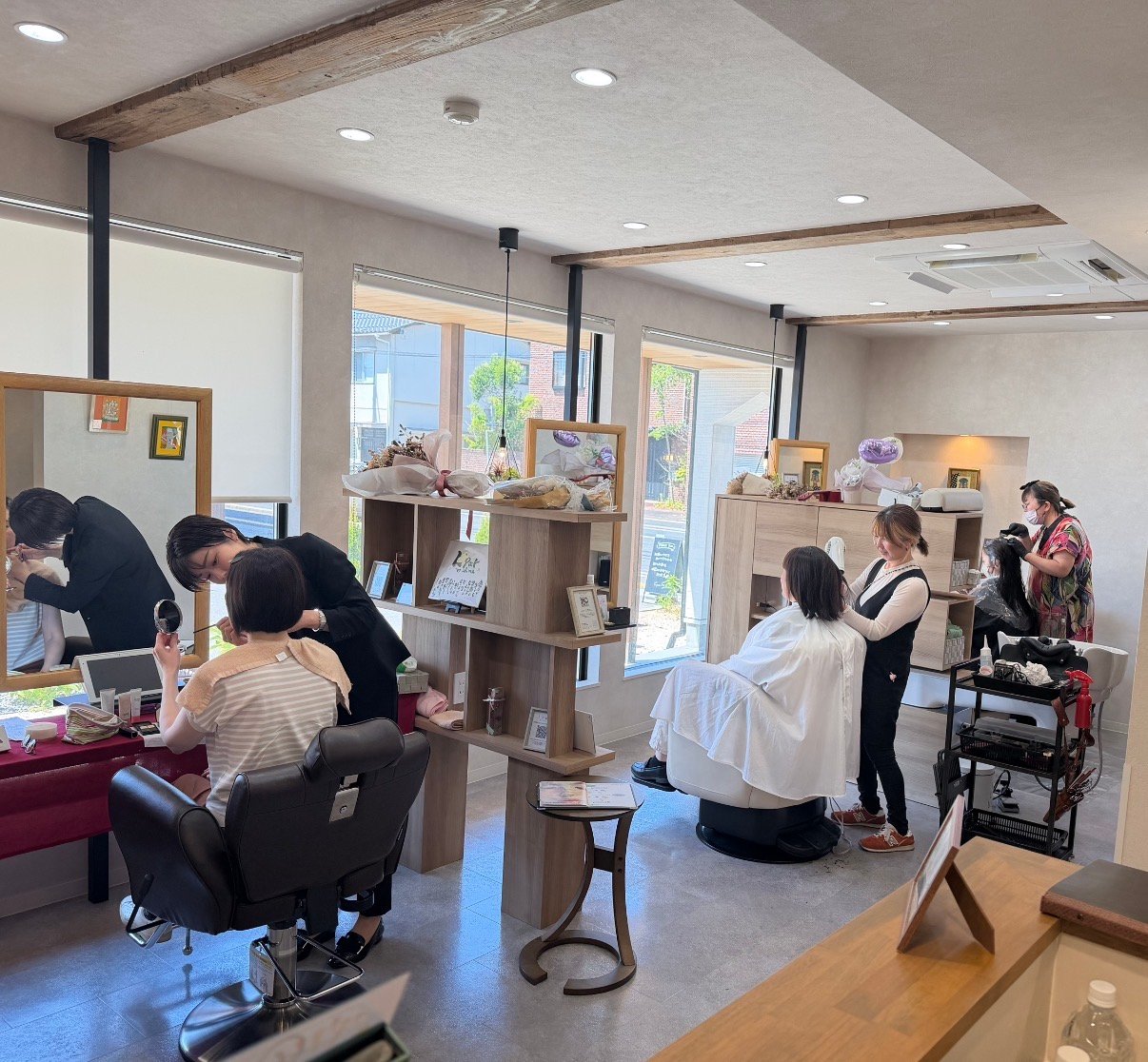 木の梁と大きな窓のある明るいサロン店内で、スタッフがお客様に施術している様子
