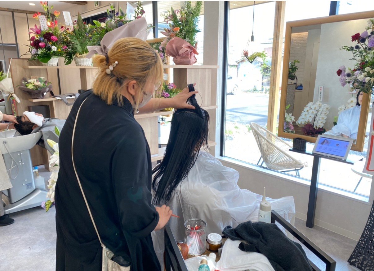 大きな窓と花に囲まれた明るい店内で、スタッフがお客様の髪を施術しているl’pur by shimaの様子